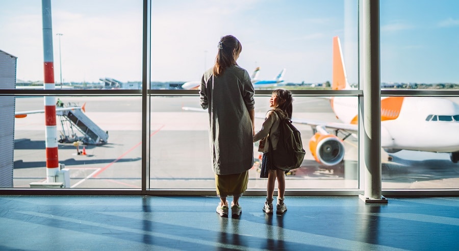 Mum and daughter watching planes through airport window.