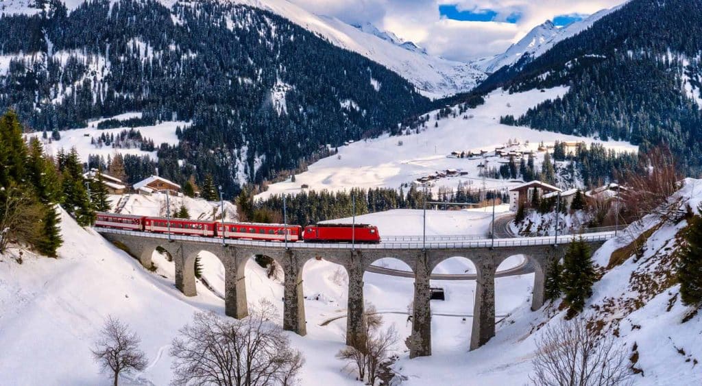 The Glacier Express crossing a bridge among a snowy landscape.