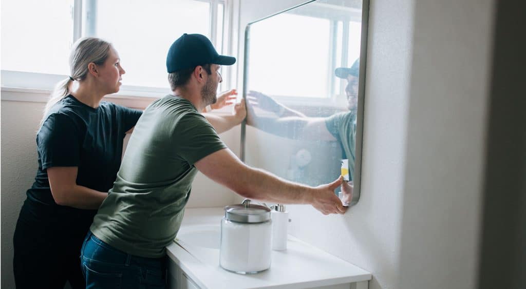 A couple installing a mirror in a bathroom