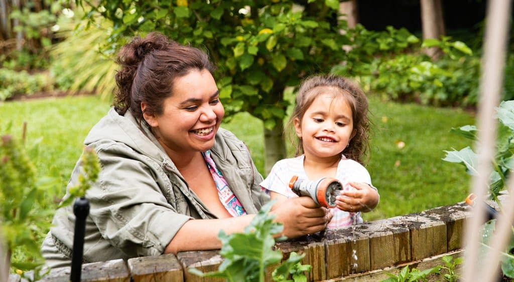 A mother and daughter watering the veggie garden in the back yard