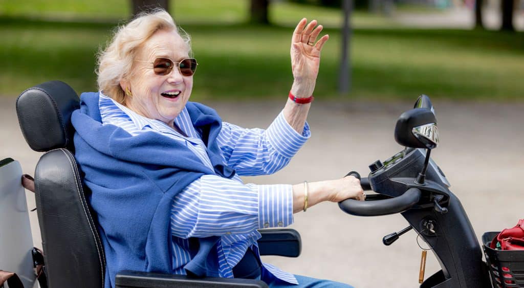 Elderly lady smiling and waving on a mobility scooter