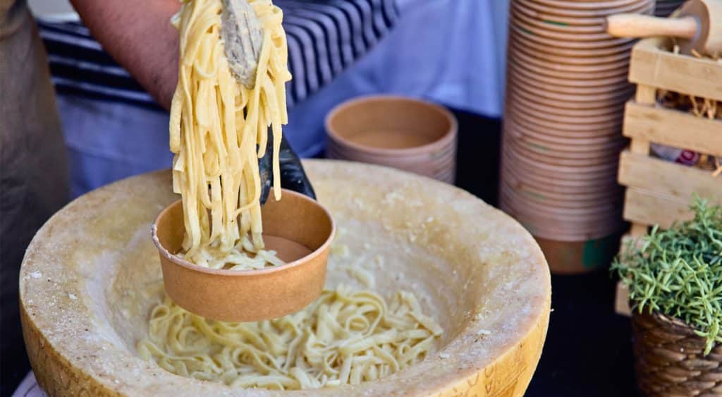 A person placing cheesy pasta in a bowl.