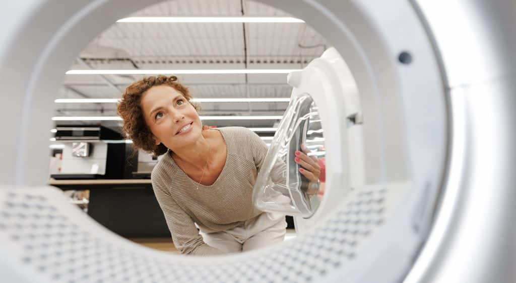 A woman looking at a front loader washing machine at an appliance store