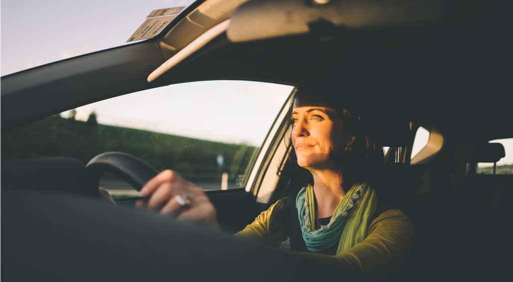 A woman behind the wheel driving at sunset