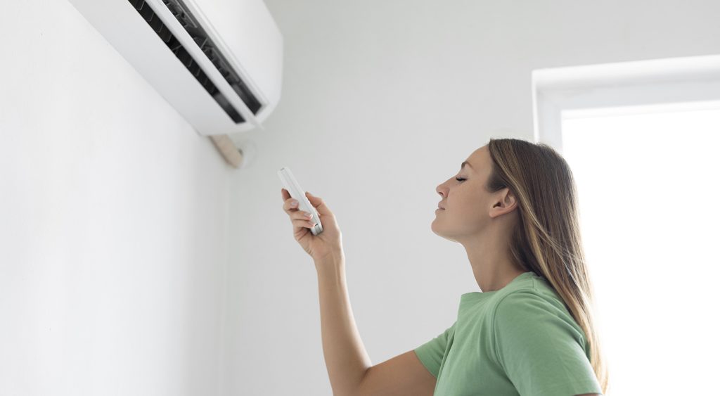 A woman turns on a split system air conditioner with a remote control
