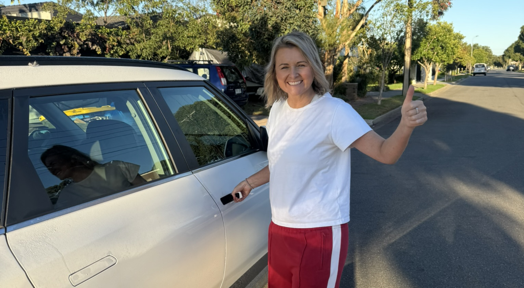 Woman next to a car giving a thumbs-up preparing to open the car door