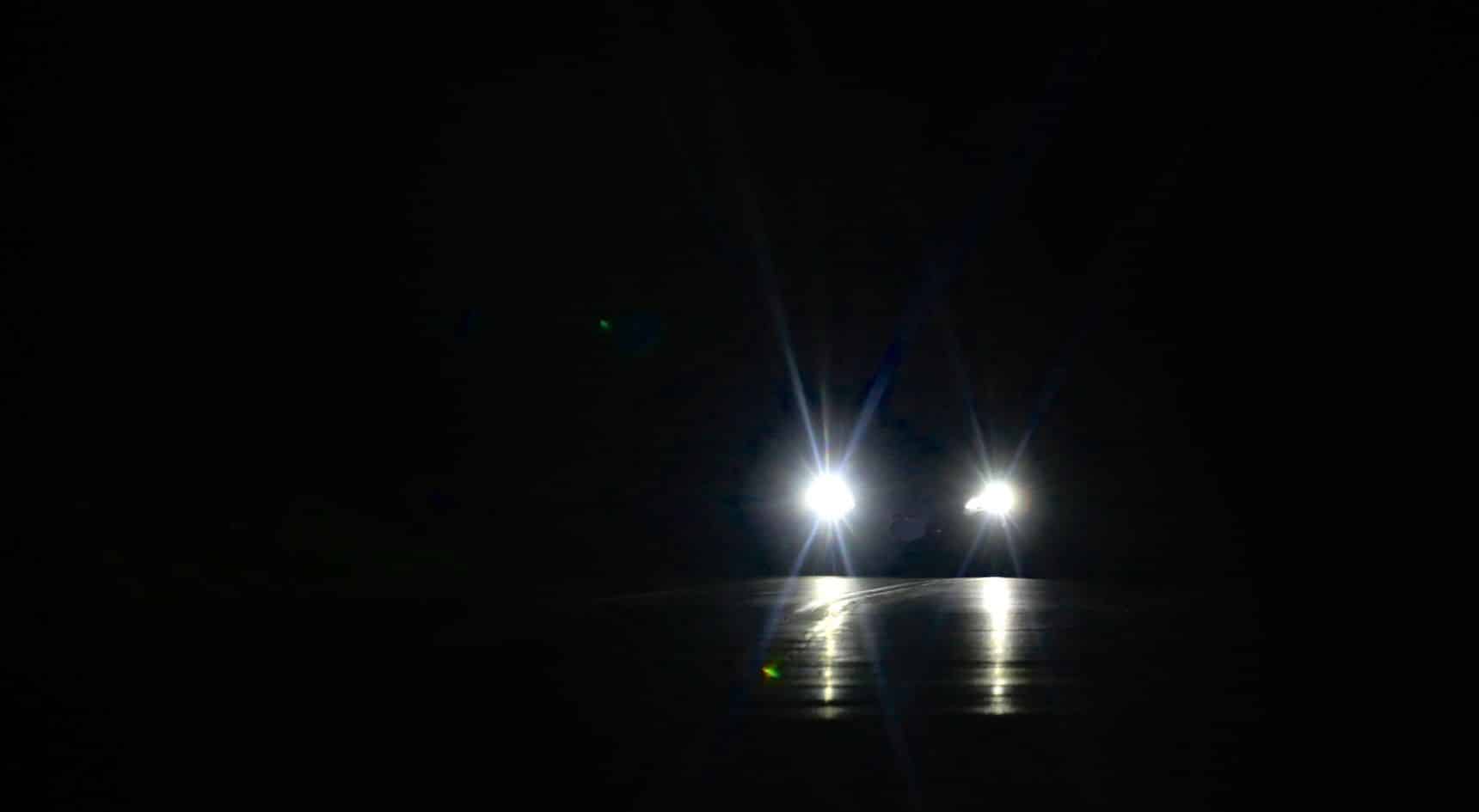 Car drives at night with headlights on.