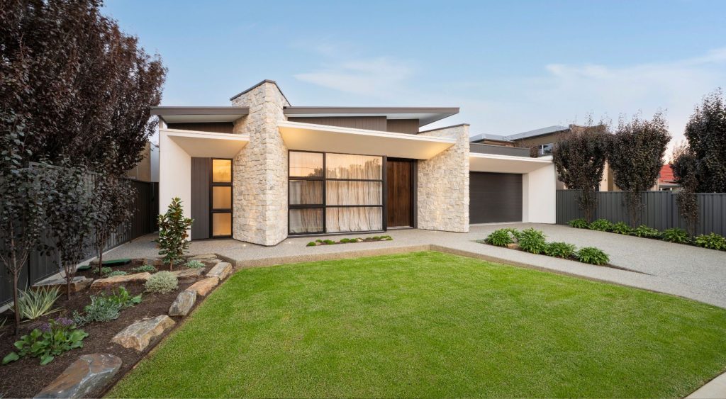Modern home with a green lawn and a paved driveway and contemporary architecture and landscaping.