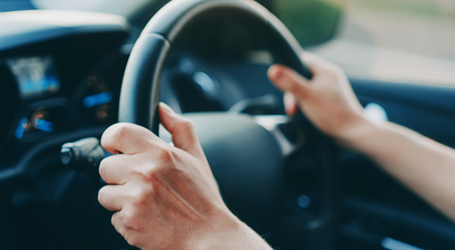 A person's hands on a steering wheel at the nine and three position.