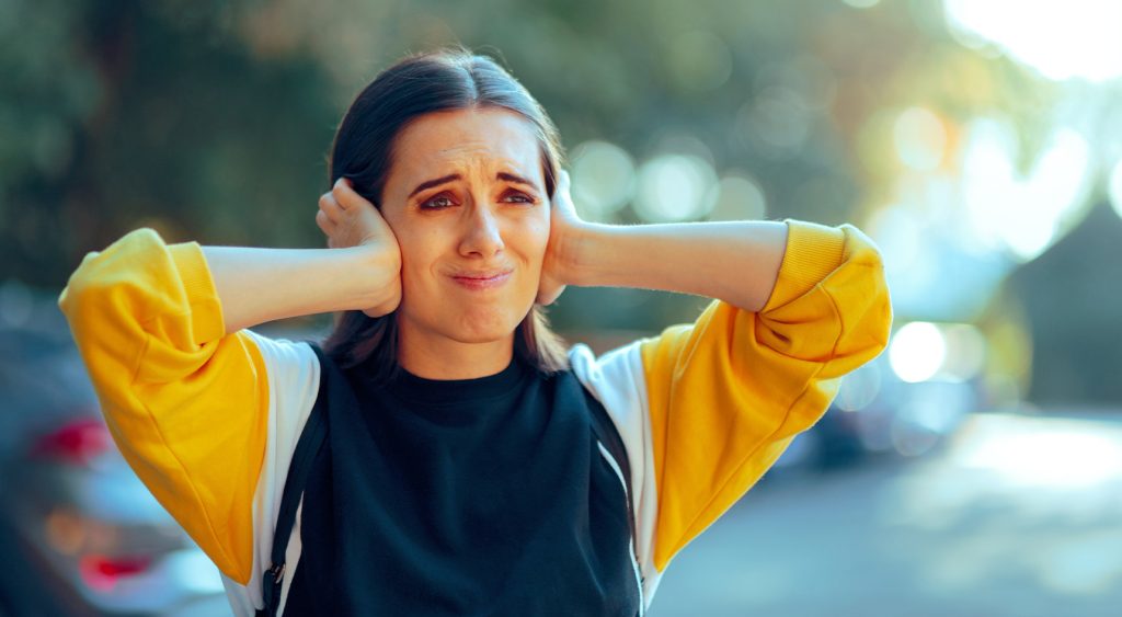 Woman covering ears in noisy street, looking upset