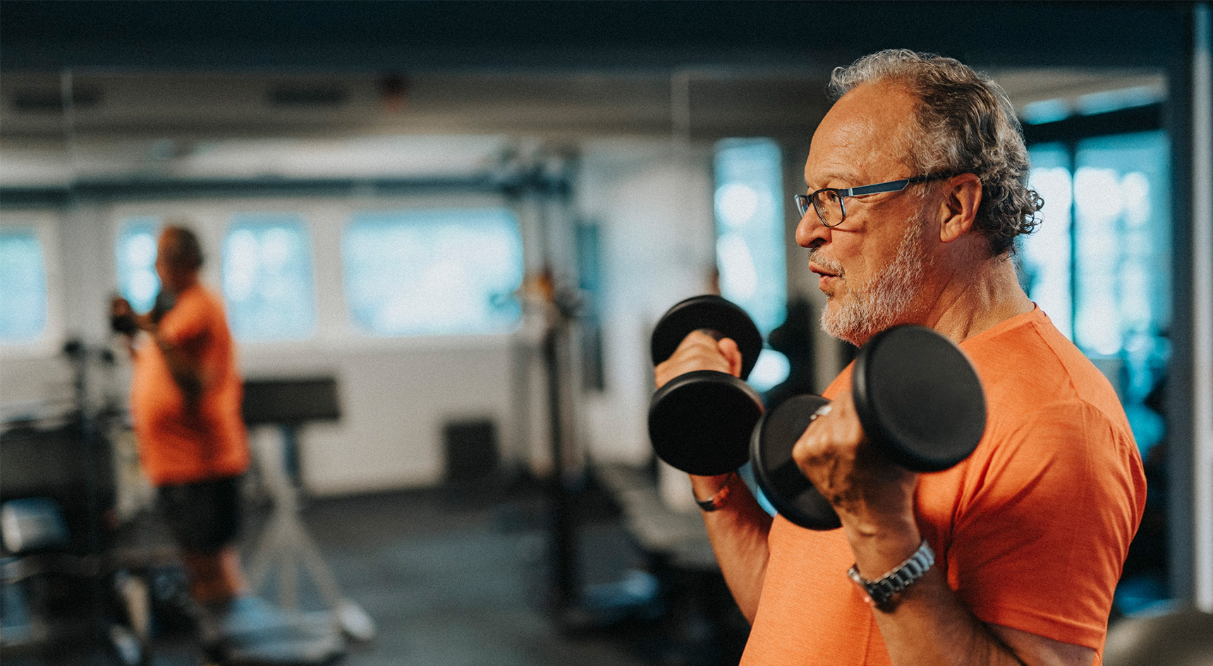Side view of active senior man with dumbbells exercising at gym