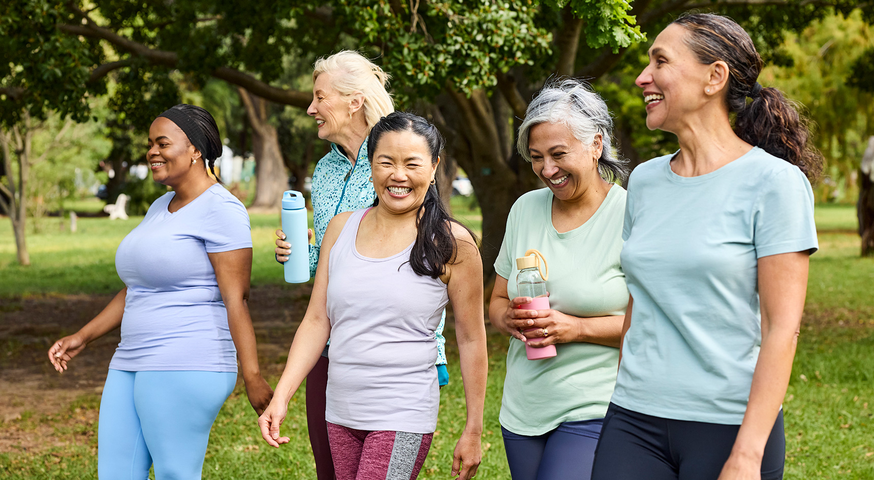Happy group of women talking with each other in park. Multiracial female friends are walking together after yoga routine. They are wearing sports clothing.