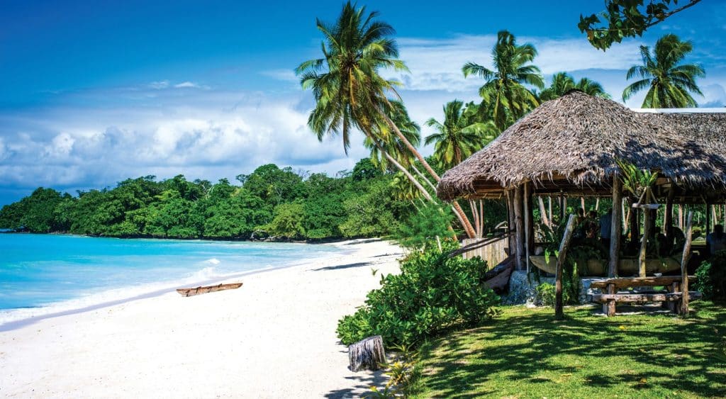 Beach with crystal blue water, white sand and a bungalow hut in Vanuatu.